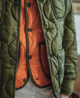 Olive quilted padded jacket close-up with snap pockets and orange inner lining