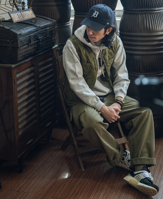 Olive quilted padded nylon vest with front pockets, worn with cap and hoodie