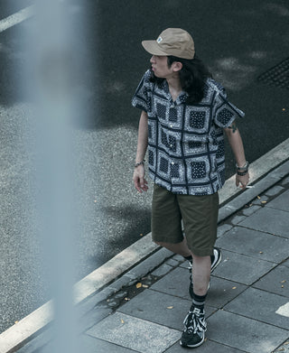 Khaki 5-panel cap with curved brim, worn with dark socks and sneakers on sidewalk