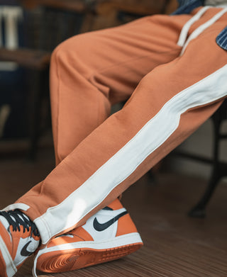 Orange sweatpants with light-blue side stripe, worn with lace-up sneakers