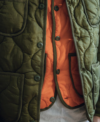 Green quilted jacket with orange padded inner vest showing black-trimmed pockets and buttons