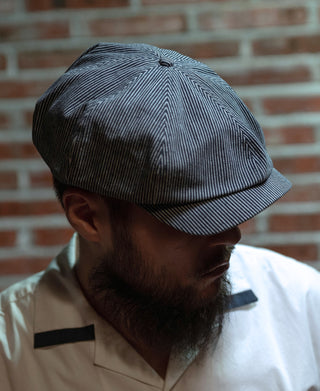 Striped denim newsboy cap worn on head, dark blue with white pinstripes and small side button.