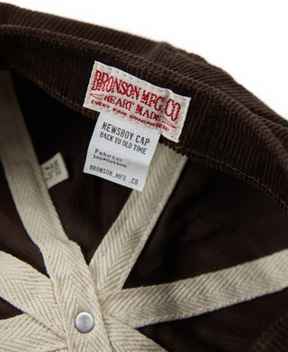 Dark brown corduroy newsboy cap with beige lining and interior logo label