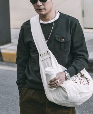 Black military pocket sweatshirt with chest pocket and brown button, worn outdoors.