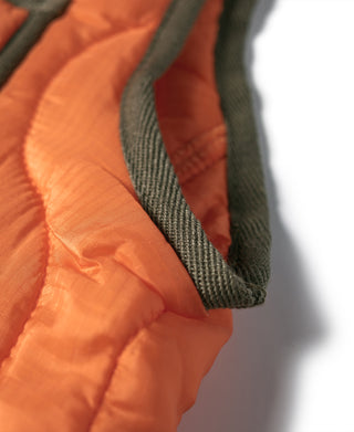 Orange ripstop vest edge detail with dark green fabric trim at neckline and armhole