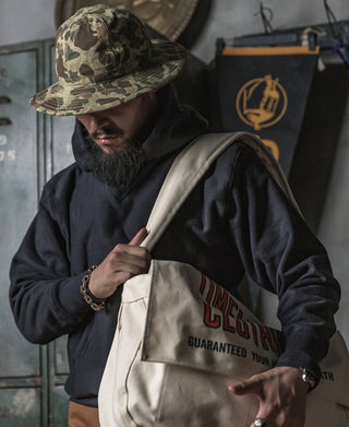 Camo bucket hat worn with hooded jacket and light-colored tote bag