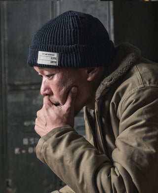 Navy ribbed knit watch cap beanie on model, small white brand label on cuff