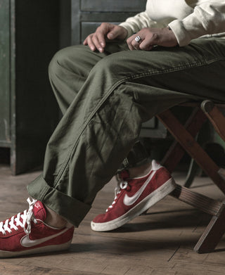Olive utility fatigue pants close-up on seated model, cuffed hem and sneakers