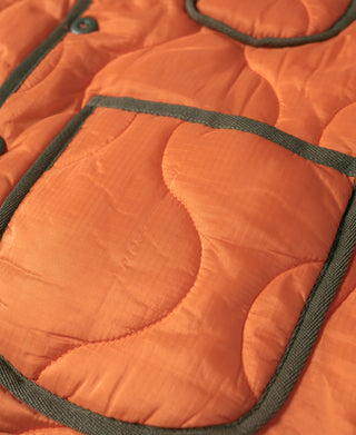 Orange quilted vest pocket detail with dark green piping and stitched ripstop texture