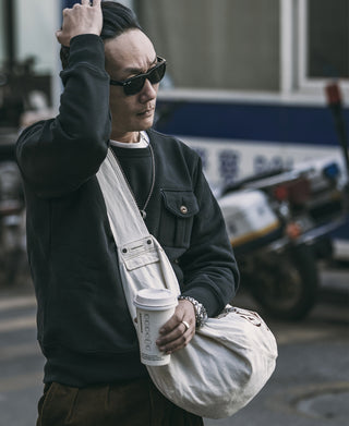 Black military pocket sweatshirt with chest pocket and ribbed cuffs, model wearing sunglasses.